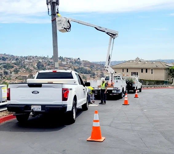 LCE Telecom field technicians performing cell tower maintenance from an aerial lift with work vehicles and safety cones on site.